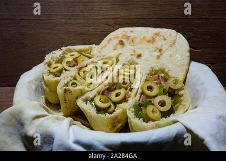 Pita o pitta focacce con verde oliva, prosciutto, aglio, cipolla, peperone verde e pomodoro in stoffa cestello, pronto a mangiare, su tavola in legno rustico Foto Stock