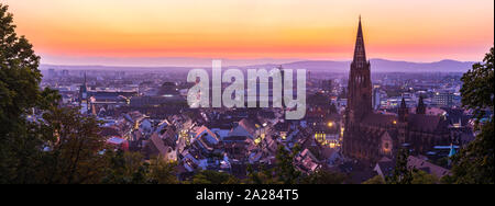 Germania, XXL panorama della skyline di Freiburg im Breisgau di notte dopo il tramonto con cielo rosso nel Magico crepuscolo da sopra Foto Stock