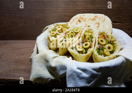 Pita o pitta focacce con verde oliva, prosciutto, aglio, cipolla, peperone verde e pomodoro in stoffa cestello, pronto a mangiare, su tavola in legno rustico Foto Stock