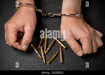 L uomo s mani in manette e munizioni su una tavola nera. Il commercio delle armi, il concetto di criminalità Foto Stock