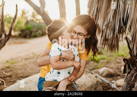 Giovane figlio abbracciando e baciando mom su roccia nel soleggiato giardino di cactus Foto Stock