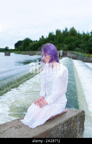 Donna seduta sulle ginocchia e nei pressi di una cascata Foto Stock