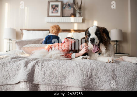 Kids giaceva sul letto con cane grande mentre la ragazza cerca di toccare i cani la linguetta Foto Stock
