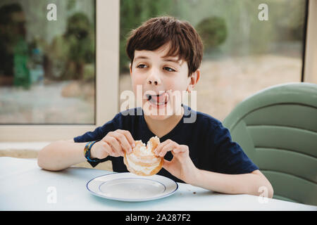 Ritratto di ragazzo con crema ciambella leccare la crema fuori la sua guancia Foto Stock