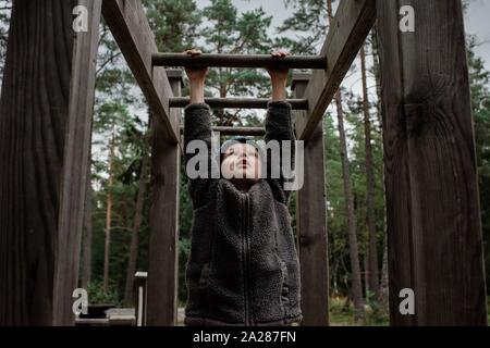 Ragazzo giocando sulle barre di scimmia arrampicata su una outdoor corso di fitness Foto Stock