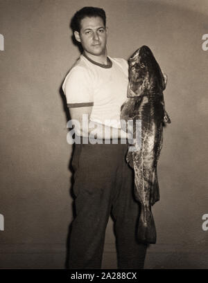 Vintage foto di un uomo in possesso di un grande pesce dei bassi, circa 1950s. Foto Stock