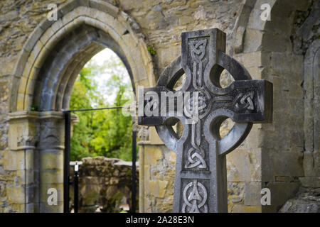 Celtic Cross tra le rovine di una Chiesa in Irlanda con un arco gotico in background. Foto Stock