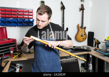 Una chitarra tecnico che sta lavorando sul fret board di una stratocaster chitarra. Lui è il controllo della fret board che si è staccata dalla chitarra Foto Stock