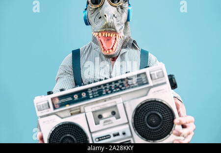 Crazy senior uomo che indossa la t-rex maschera e ascolto di musica tenendo vintage stereo boombox outdoor - moda maschile masquerade avente fun dancing Foto Stock