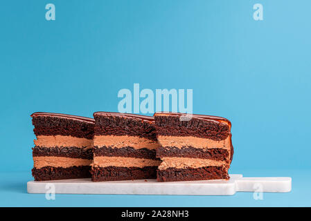 Cioccolato torta stratificata fetta allineate e visualizzati su un taglio bianco bordo e sfondo blu. Torta di compleanno pezzi. Tre porzioni di torta di festa Foto Stock