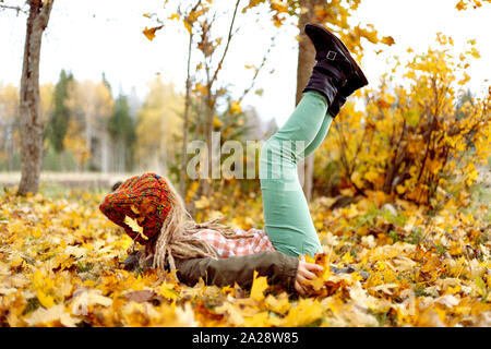 Ragazza cadde in giallo dorato di foglie di acero e si diverte in foglie di acero in autunno. Foto Stock