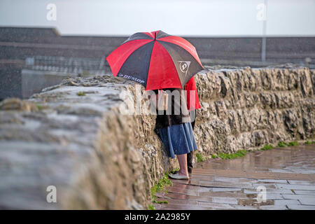 Porthcawl, South Wales, Regno Unito. 1 Ottobre 2019 - Porthcawl - REGNO UNITO : Persone riparo sotto il loro ombrello durante una doccia a pioggia a Sandy Bay in Porthcawl questa sera. Credito: Phil Rees/Alamy Live News Foto Stock