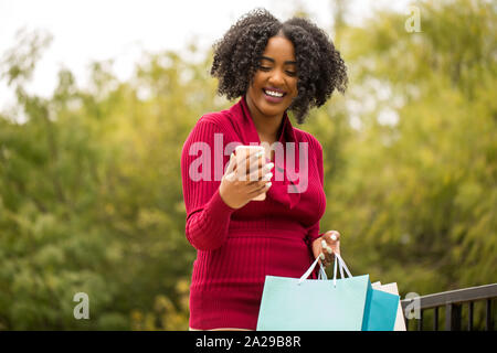 Bella americano africano donna shopping e i messaggi di testo. Foto Stock