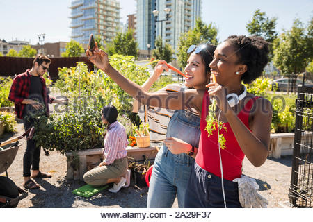 Giocoso donne giovani amici con le carote tenendo selfie con la fotocamera del telefono nella soleggiata, urban comunità giardino