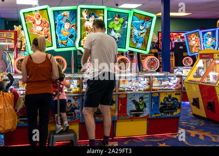 Una giovane famiglia giocando due penny slot machines o moneta spingere il gioco in un divertimento arcade Foto Stock