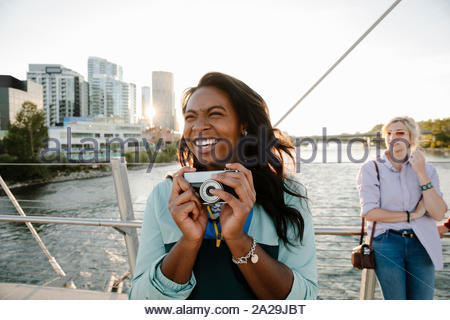 Giocoso giovane donna con fotocamera retrò sul soleggiato, ponte urbano