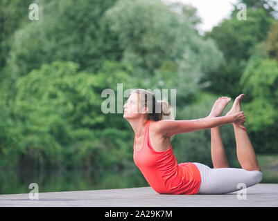 Donna nella sua Anni Trenta facendo Yoga nel Parco su un molo Foto Stock