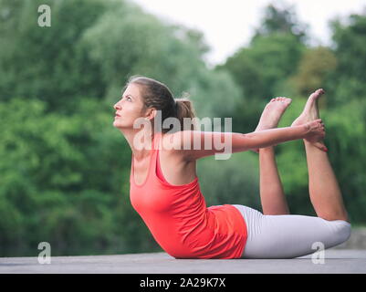 Donna nella sua Anni Trenta facendo Yoga nel Parco su un molo Foto Stock