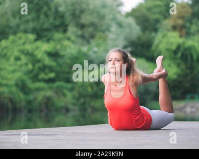 Donna nella sua Anni Trenta facendo Yoga nel Parco su un molo Foto Stock