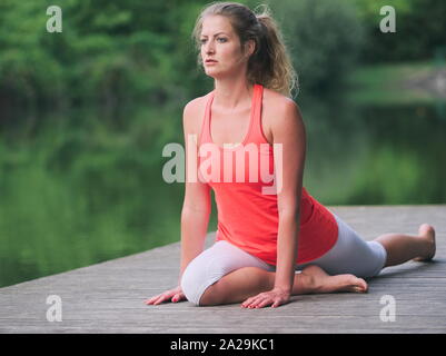 Donna nella sua Anni Trenta facendo Yoga nel Parco su un molo Foto Stock