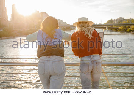 Giovani donne amici guardando il fiume dalla soleggiata, ponte urbano