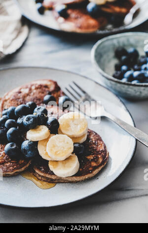 Un sano comfort colazione set. Flat-lay di banana pancake con mirtilli freschi e miele in piastre su marmo bianco sullo sfondo della tabella Foto Stock