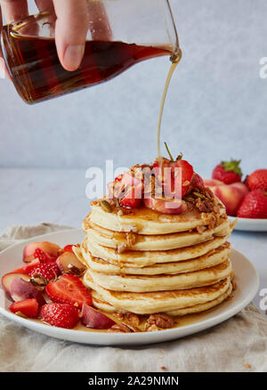 Versare lo sciroppo di acero sopra una pila di American pancake con Stawberries e pesche Foto Stock