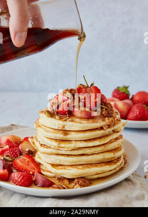 Versare lo sciroppo di acero sopra una pila di American pancake con Stawberries e pesche Foto Stock