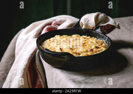 Americano classico piatto cotto mac e formaggio in ghisa pan con asciugamano sul tavolo da cucina con tovaglie di lino. Dark rustik style Foto Stock