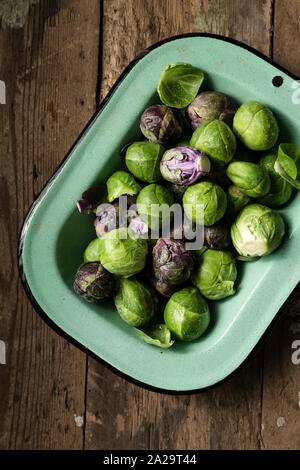 Materie i cavoletti di Bruxelles in un vintage, smalto verde piatto su un rustico di una superficie di legno. Foto Stock