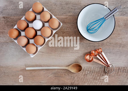 Bianco di ceramica vassoio contenente undici marrone e uno bianco uovo e utensili di cottura nel piatto composizione laici sul legno rustico sfondo. Mangiare sano co Foto Stock