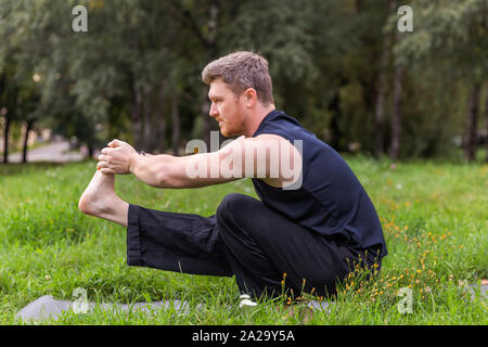 Ispirato uomo fare yoga asana nel parco della città. Centro Fitness all'aperto e di vita il concetto di equilibrio. Foto Stock