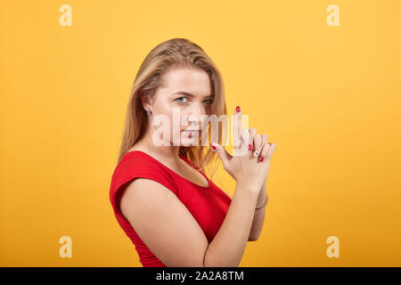 Giovane ragazza bionda in t-shirt rossa isolato su sfondo arancione mostra le emozioni Foto Stock