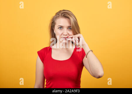 Giovane ragazza bionda in t-shirt rossa isolato su sfondo arancione mostra le emozioni Foto Stock