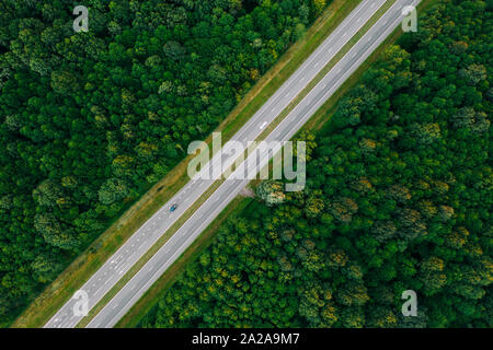 Vista aerea dell'autostrada strada attraverso il verde paesaggio forestale in estate. Vista superiore vista piana della autostrada Autostrada superstrada dall atteggiamento di alta. Viaggio e Trav Foto Stock