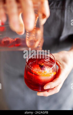 Una donna con un tatuato il braccio sinistro si riversa il Negroni cocktail in un piccolo bicchiere Foto Stock