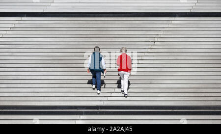 Due donne anziane vestito di rosso e blu salendo su grande scala. Foto Stock