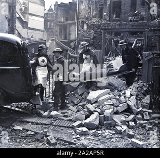 1940, storico, Londra durante il blitz, due volontari maschi operai che trasportano un civile paziente su una barella da una bomba edificio danneggiato nel retro di un furgone a seguito di un raid aereo, accompagnato dal MMU infermieri, Durante WW2, Inghilterra, Regno Unito. Foto Stock