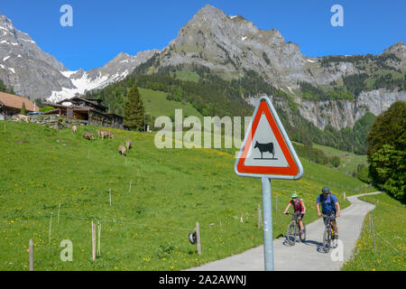 Engelberg, Svizzera - 3 Giugno 2019: persone in mtb nella parte anteriore di una mucca cartello stradale a Engelberg sulle alpi svizzere Foto Stock