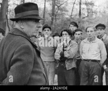 Un uomo anziano si erge davanti a un gruppo di giovani uomini. Due generazioni si fronteggiano in modo sospetto. Immagine non datata. Foto Stock