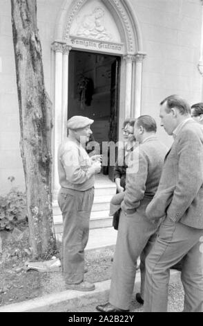 Foto di alcuni visitatori e giornalisti nel Ostfriedhof del Comune di Montelepre in provincia di Palermo (Regione Sicilia). Un uomo locale sta parlando ai visitatori di fronte alla tomba. Ex eroe popolare Salvatore Giuliano (anche nato a Montelepre) è sepolta nel cimitero. Egli è stato per lungo tempo considerato come una sorta di 'Sicilian Robin Hood", ma ha anche avuto collegamenti con la mafia. Foto Stock