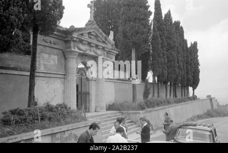 Foto di alcuni visitatori e giornalisti nel Ostfriedhof del Comune di Montelepre in provincia di Palermo (Regione Sicilia). Un uomo locale sta parlando ai visitatori di fronte alla tomba. Ex eroe popolare Salvatore Giuliano (anche nato a Montelepre) è sepolta nel cimitero. Egli è stato per lungo tempo considerato come una sorta di 'Sicilian Robin Hood", ma ha anche avuto collegamenti con la mafia. Foto Stock