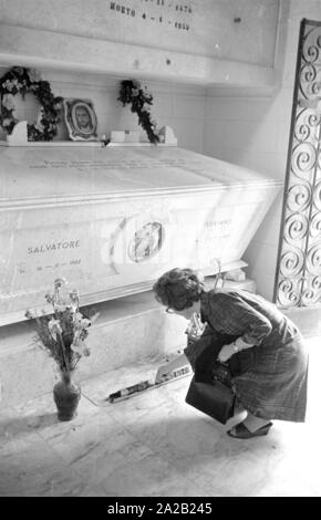 Foto della bara di Salvatore Giuliano nel Ostfriedhof del Comune di Montelepre in provincia di Palermo (Regione Sicilia). Una donna candele luci nella parte anteriore di essa. Ex eroe popolare Salvatore Giuliano (anche nato a Montelepre) è sepolta nel cimitero. Egli è stato per lungo tempo considerato come una sorta di 'Sicilian Robin Hood", ma ha anche avuto collegamenti con la mafia. Foto Stock