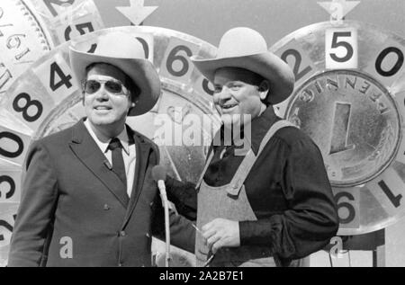 Wim Thoelke e il impersonator di Hoss dalla serie televisiva Bonanza, Dan Blocker, in show televisivo 3x9. Il fortunato ruote nella forma del marchio tedesco e il Pfenning sono i simboli della Aktion Sorgenkind. Foto Stock