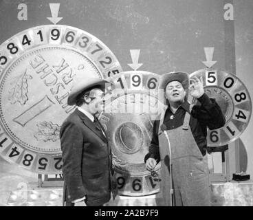 Wim Thoelke e il impersonator di Hoss dalla serie televisiva Bonanza, Dan Blocker, in show televisivo 3x9. Il fortunato ruote nella forma del marchio tedesco e il Pfenning sono i simboli della Aktion Sorgenkind. Foto Stock