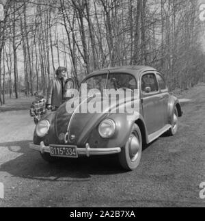 Una donna con il bambino presso la porta del passeggero di un standard VW bavarese con numero di targa. Foto Stock