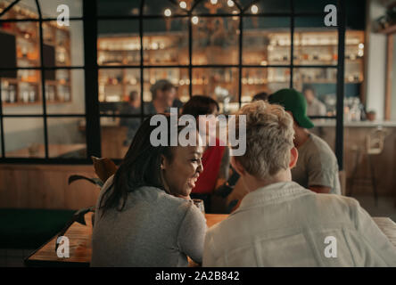 Due donne ridere mentre è seduto con gli amici in un bar Foto Stock
