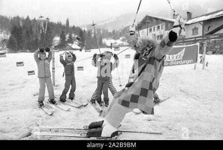 Bambini a un corso di sci della Skischule Garmisch. Il maestro di sci è un clown. La società marker" annuncia la sua sicurezza attacchi da sci con striscioni. Foto Stock