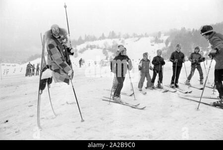 Bambini a un corso di sci della Skischule Garmisch con un clown come maestro di sci. La società marker" annuncia la sua sicurezza attacchi da sci con striscioni. Foto Stock