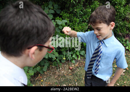 Due bambini di scuola in uniforme scolastica giocando una partita di conkers avente un conker lotta al di fuori in autunno 2019 Foto Stock